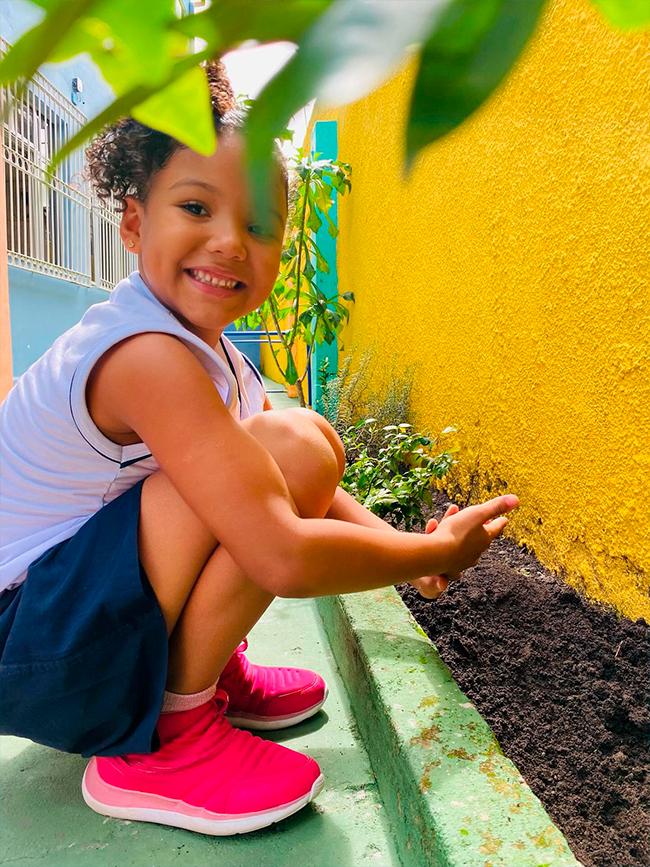 Aluna dos Anos Iniciais cuidando do canteiro da horta do Colégio Arte de Aprender
