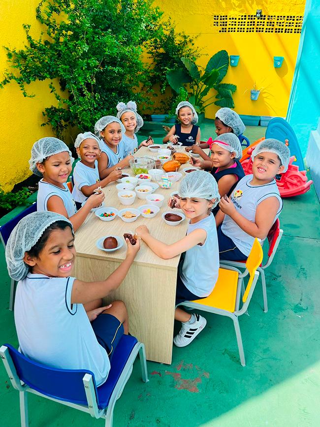 Turma do Ensino Fundamental reunida à mesa em atividade de cozinha experimental no pátio da escola