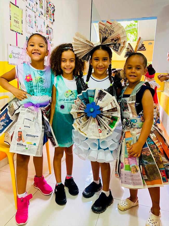 Alunas do Ensino Fundamental apresentando peças criadas com material reciclado em projeto de meio ambiente